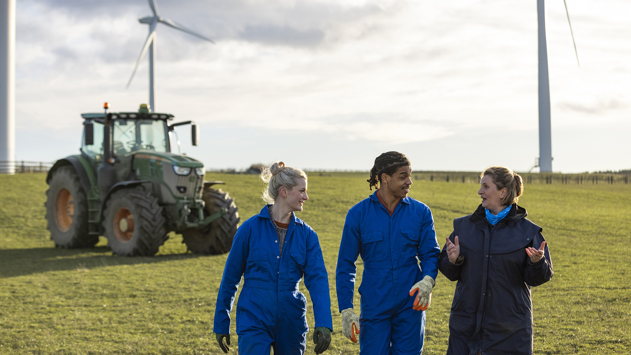 Three famers walk in a field in Northumberland with wind turbines in the distance.